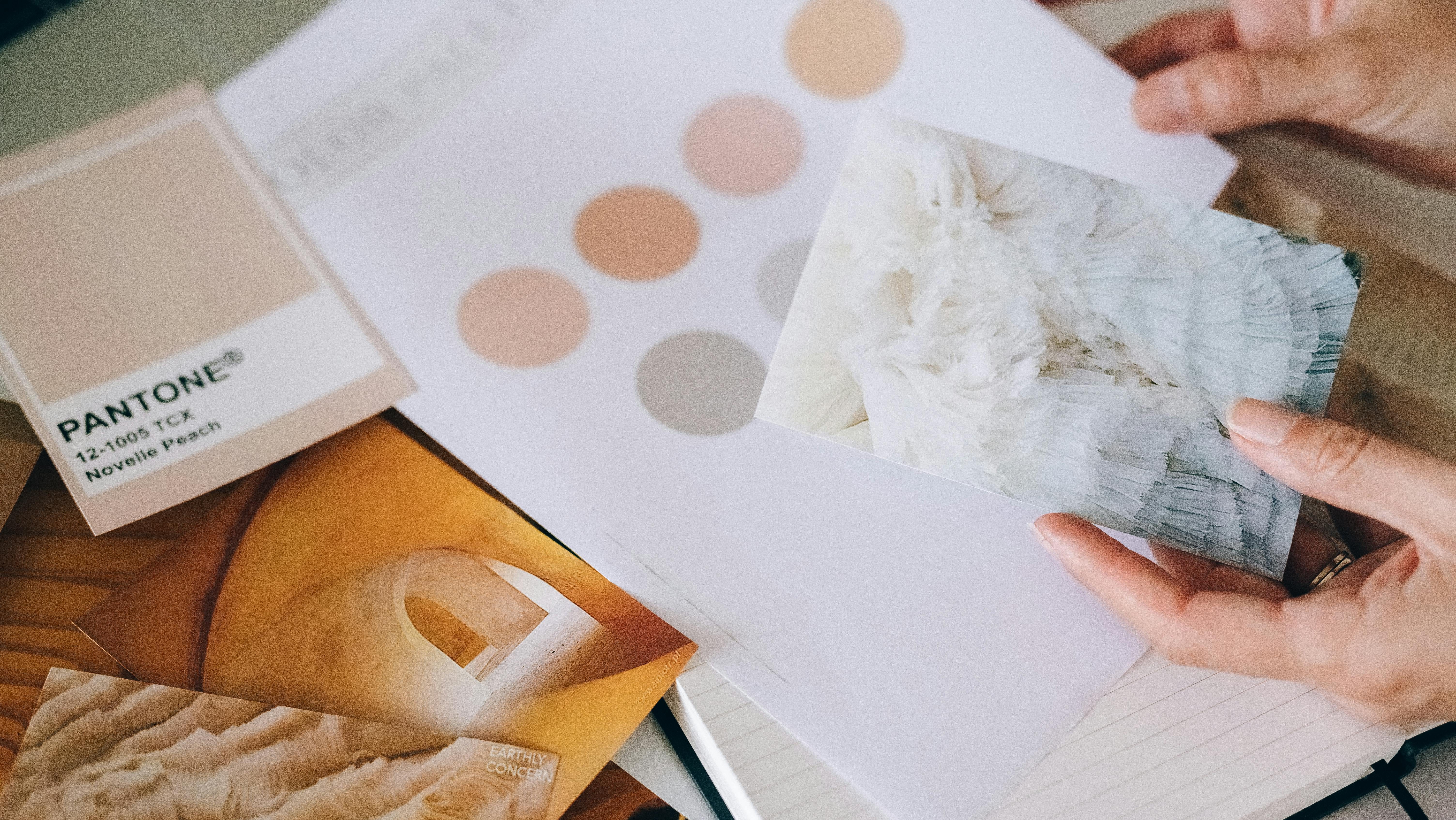 A photograph of a pantone swatch, colour samples and two hands holding a picture of fabric