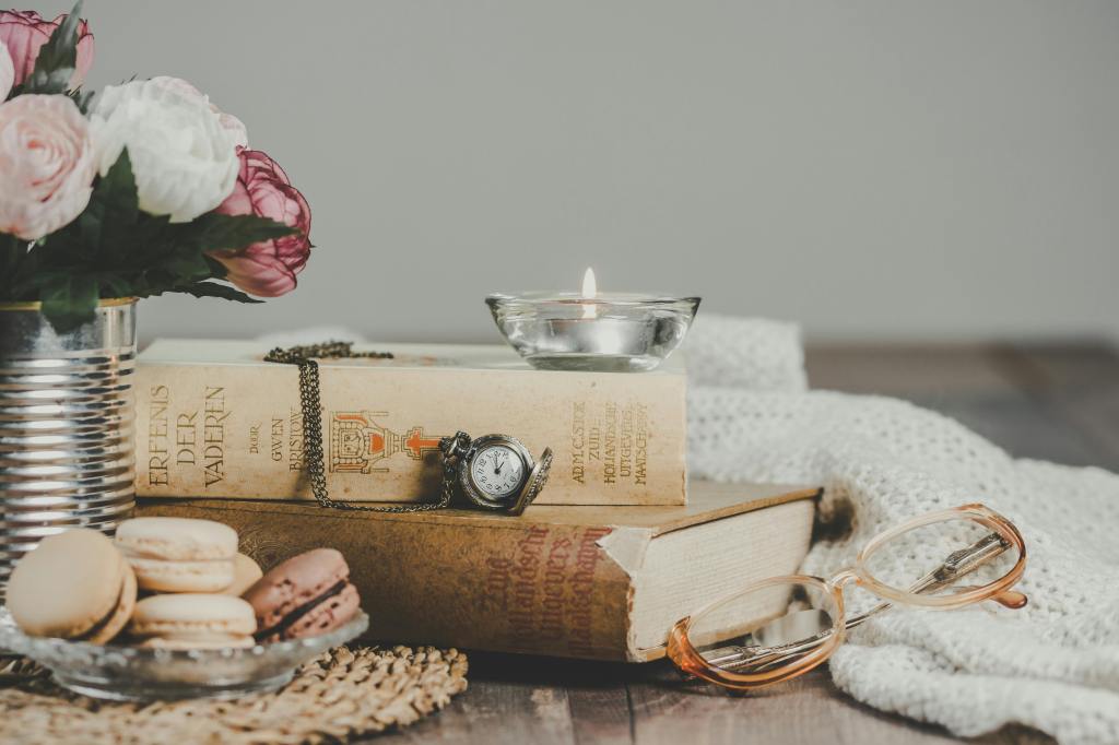 A photograph of some books, flowers and a candle